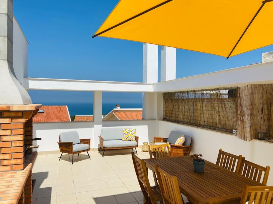 eine Terrasse mit einem Tisch und Stühlen sowie einem gelben Regenschirm in der Unterkunft Ocean Terrace - Private Patio with BBQ & Sea view in Nazaré