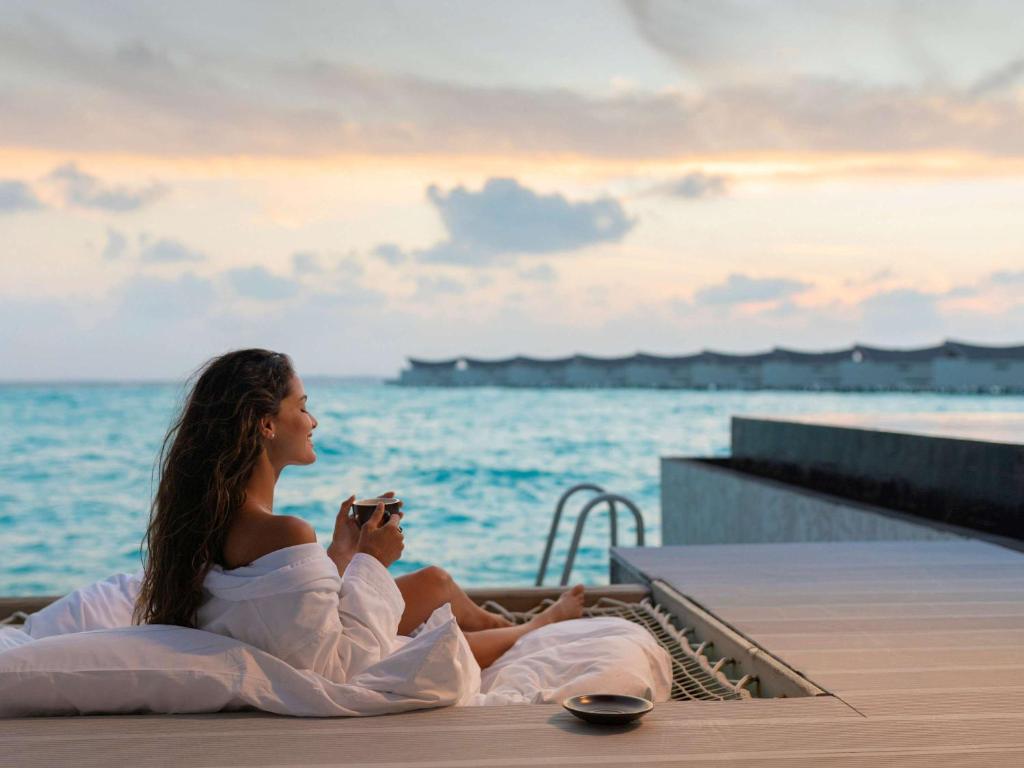 a woman sitting on the edge of a pool overlooking the ocean at Mӧvenpick Resort Kuredhivaru Maldives in Manadhoo