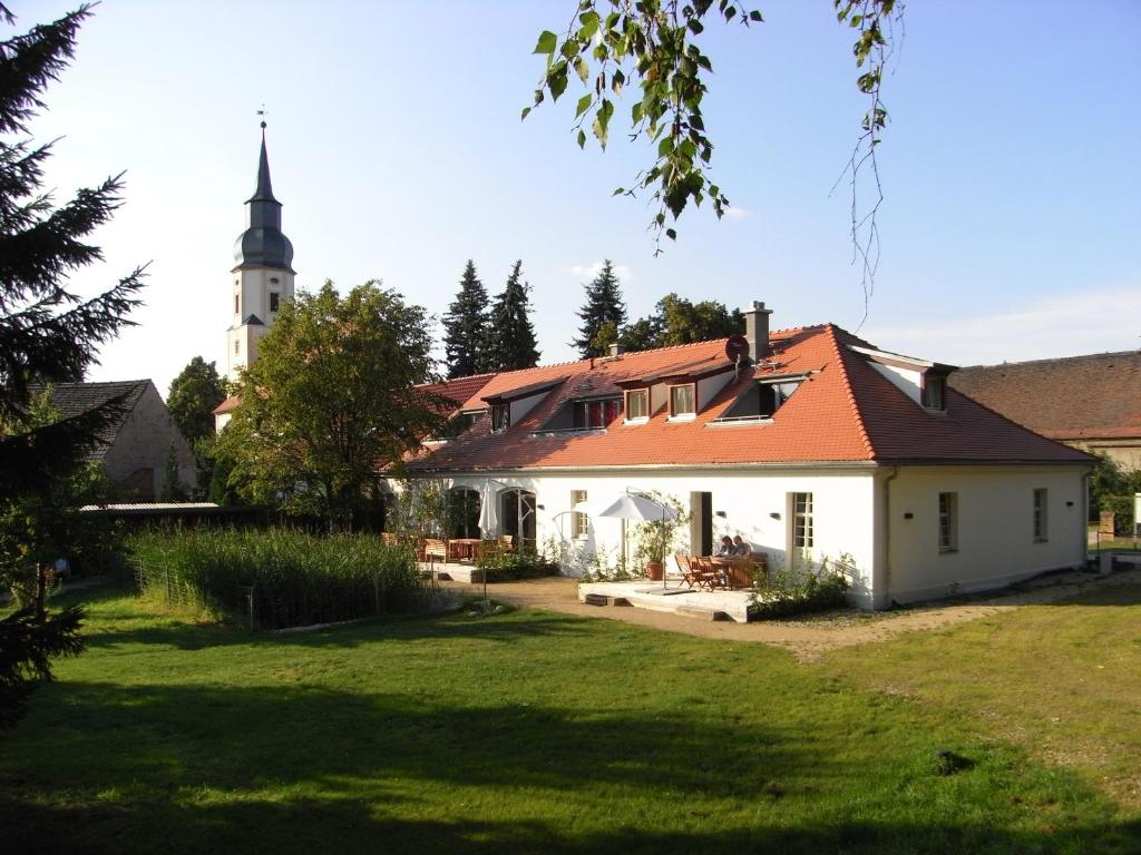 a white house with an orange roof and a church at Apartmenthotel "Gärtnerhaus Schloss Reinharz" in Bad Schmiedeberg