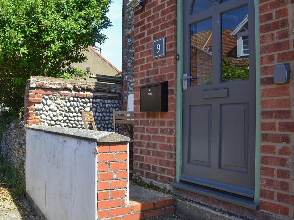 a brick house with a blue door and a stone wall at Avocet Cottage in Sheringham