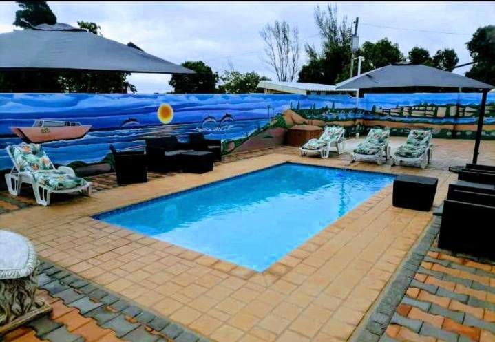 a large swimming pool with chairs and an umbrella at Sekos Guest House & Shisanyama in St Lucia
