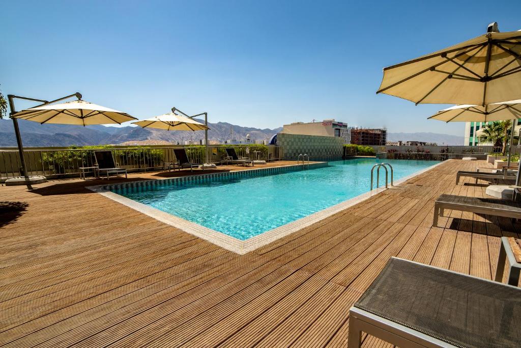 uma piscina com cadeiras e guarda-sóis num deque em Millennium Executive Apartments Muscat em Mascate