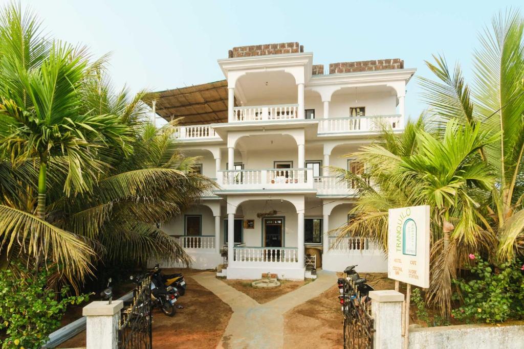 a large white building with palm trees in front of it at Tranquilo Arambol in Arambol