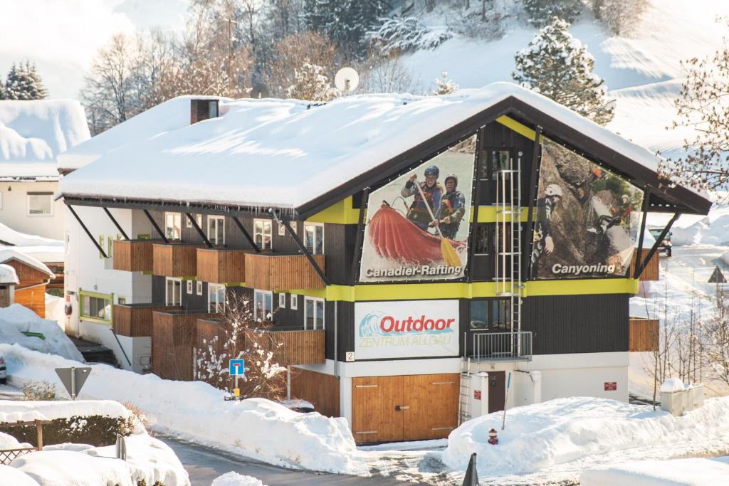 Un edificio cubierto de nieve con una valla publicitaria en él. en Outdoor Zentrum Allgäu- Hostel, en Bihlerdorf