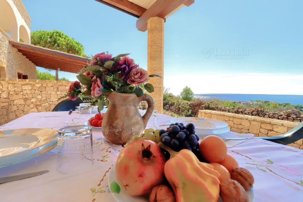 stół z talerzem owoców i wazonem kwiatów w obiekcie Case Vacanze San Gregorio by LoveSud w mieście Patù