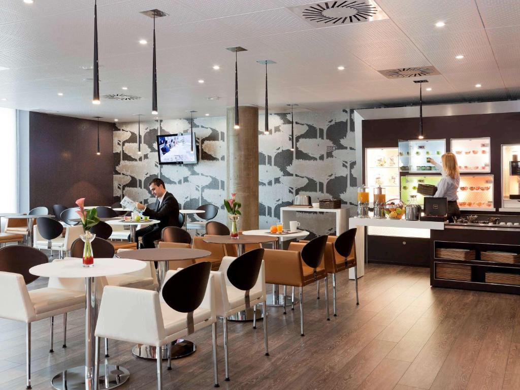 a restaurant with tables and chairs and a person in the background at Novotel Suites Malaga Centro in Málaga