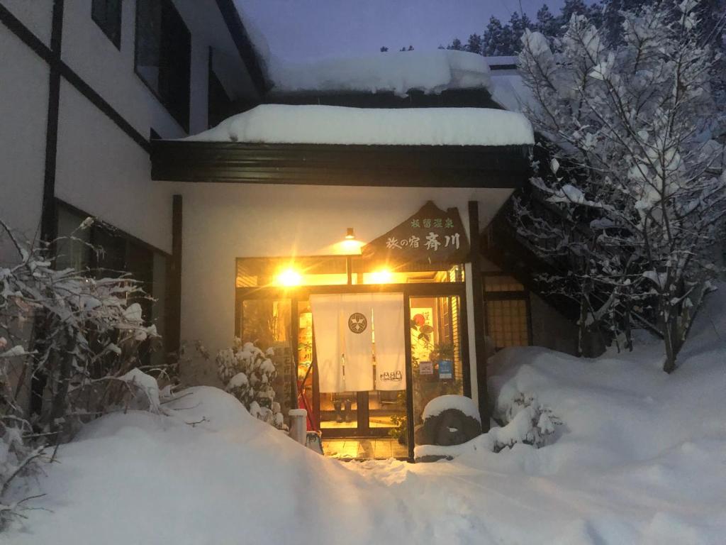 una casa cubierta de nieve con una luz en la puerta en Tabinoyado Saikawa en Kuroishi