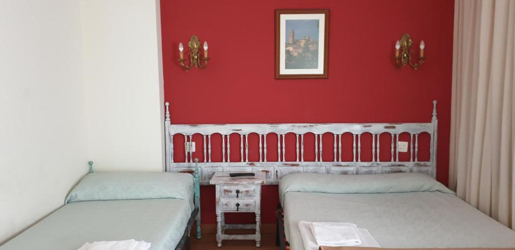 two beds in a room with a red wall at Las Brasas De Eddy in La Lastrilla