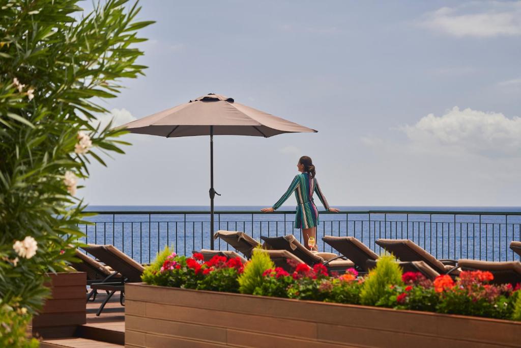 a woman standing under an umbrella on the beach at The Cliff Bay - PortoBay in Funchal