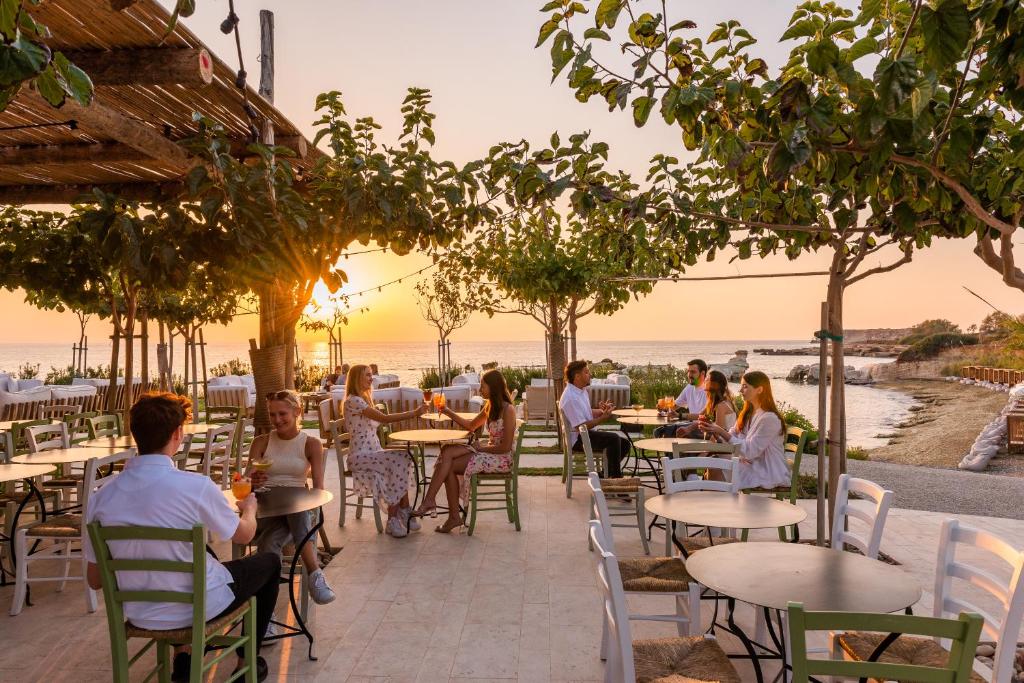 a group of people sitting at tables at a restaurant on the beach at Cap St Georges Villas in Peyia