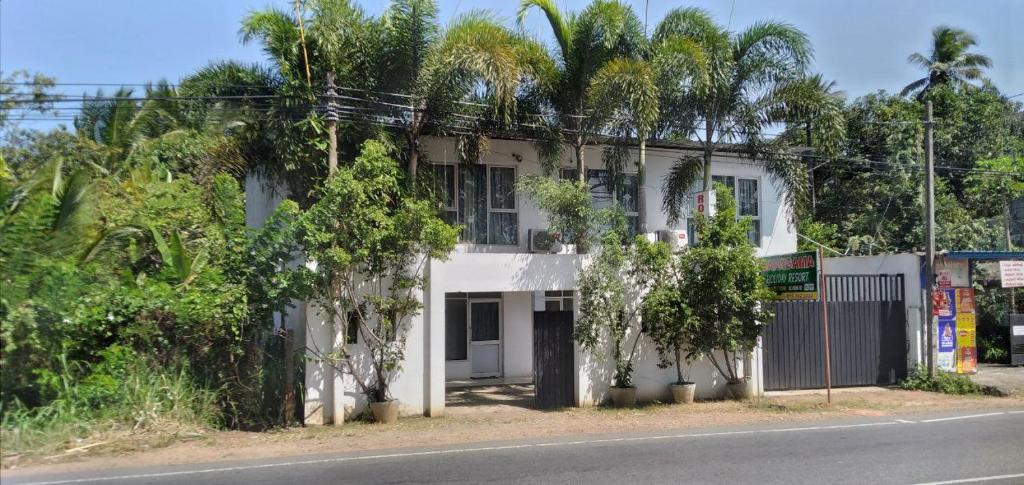 biały budynek z drzewami po stronie drogi w obiekcie Saragama Holiday Resort w mieście Kurunegala