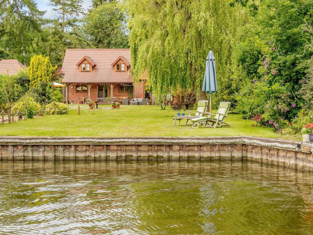 a house with an umbrella and chairs next to a river at Riversdale Cottage in Neatishead