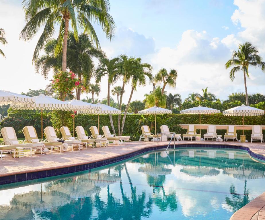 ein Pool mit Stühlen und Sonnenschirmen und Palmen in der Unterkunft The Colony Hotel in Palm Beach