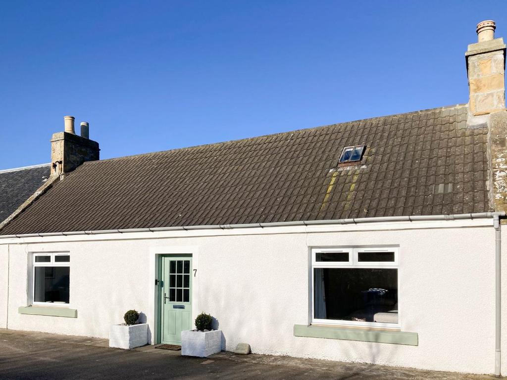 a white building with a brown roof and two windows at Fishers Cottage in Balintore