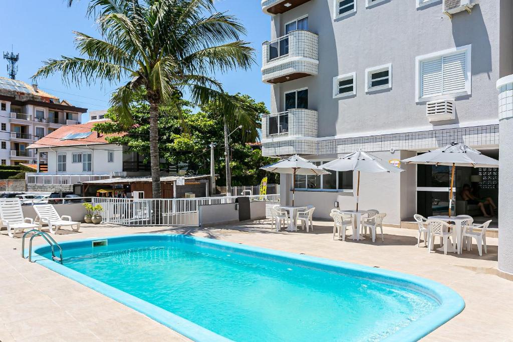a swimming pool in front of a building with chairs and umbrellas at Prédio com apartamentos completos, com piscina e a passos da praia - Agua Marinha in Florianópolis