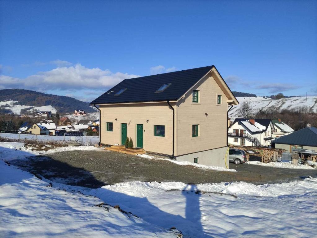 une maison avec un toit noir dans la neige dans l'établissement Apartamenty Dubacik, à Tylicz