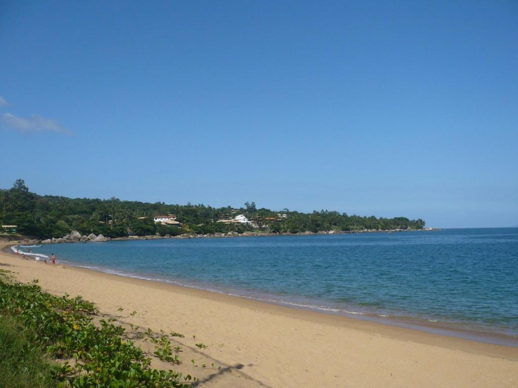 uma praia com água azul e árvores ao fundo em CHALÉ da LÚ ILHABELA em Ilhabela