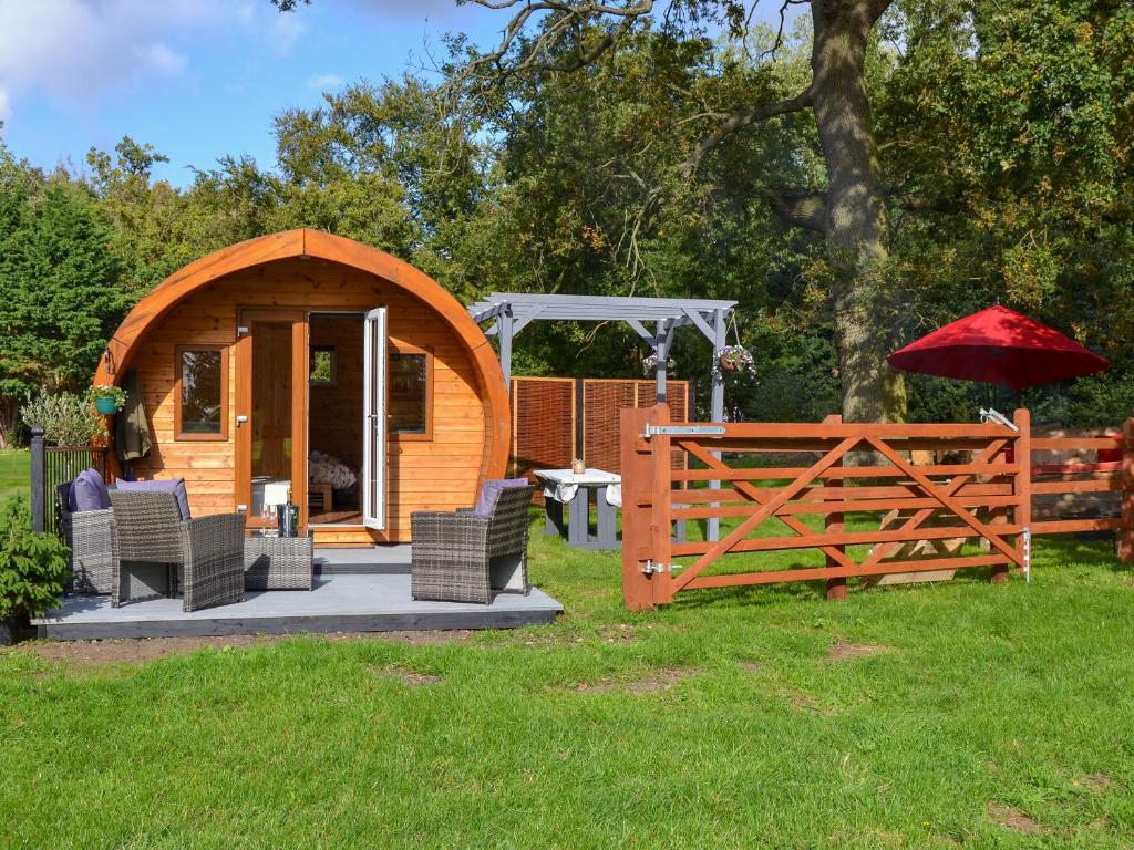 a wooden cabin with chairs and a red umbrella at Park View - Ukc4925 in Roydon