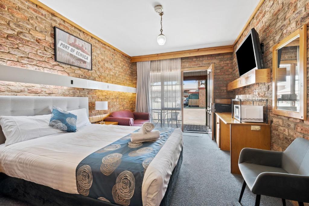 1 dormitorio con 1 cama grande y pared de ladrillo en The Settlement Historic Hotel en Echuca