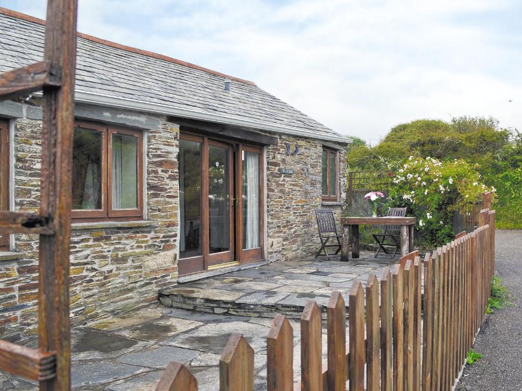 a stone cottage with a wooden fence and a table at Wild Rose in Delabole