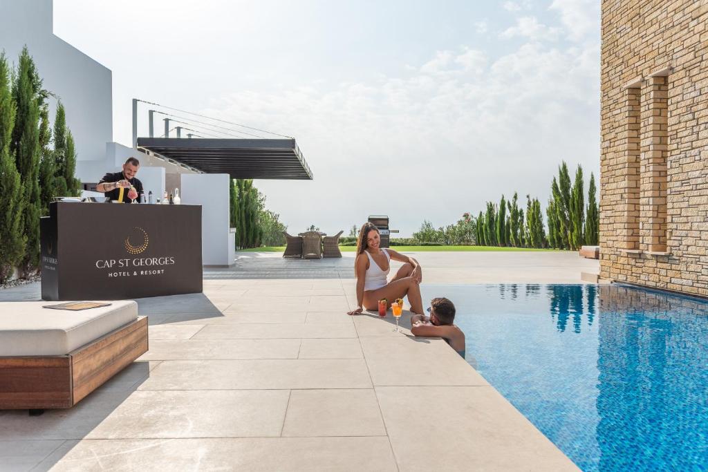 a woman and a child sitting next to a swimming pool at Cap St Georges Villas in Peyia