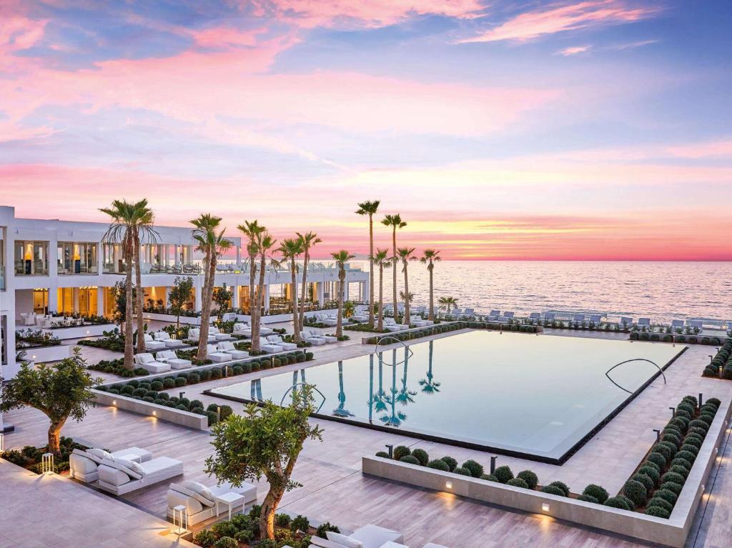 une image d'une piscine avec des palmiers et l'océan dans l'établissement Grecotel LUX.ME White Palace​, à Adelianos Kampos