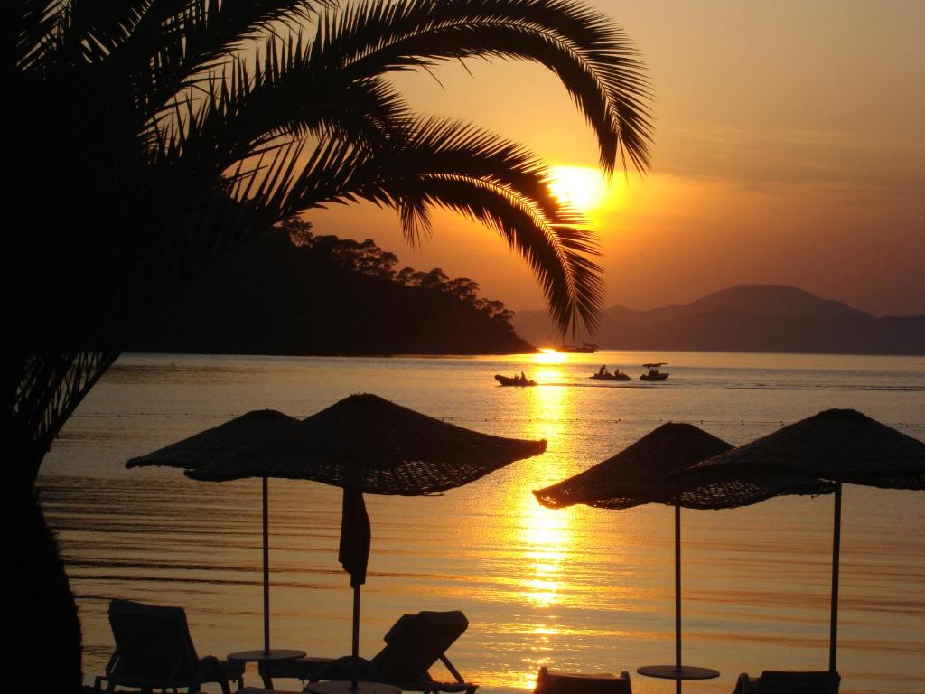 un tramonto su una spiaggia con sedie e ombrelloni di Lighthouse Legend Aparts a Fethiye