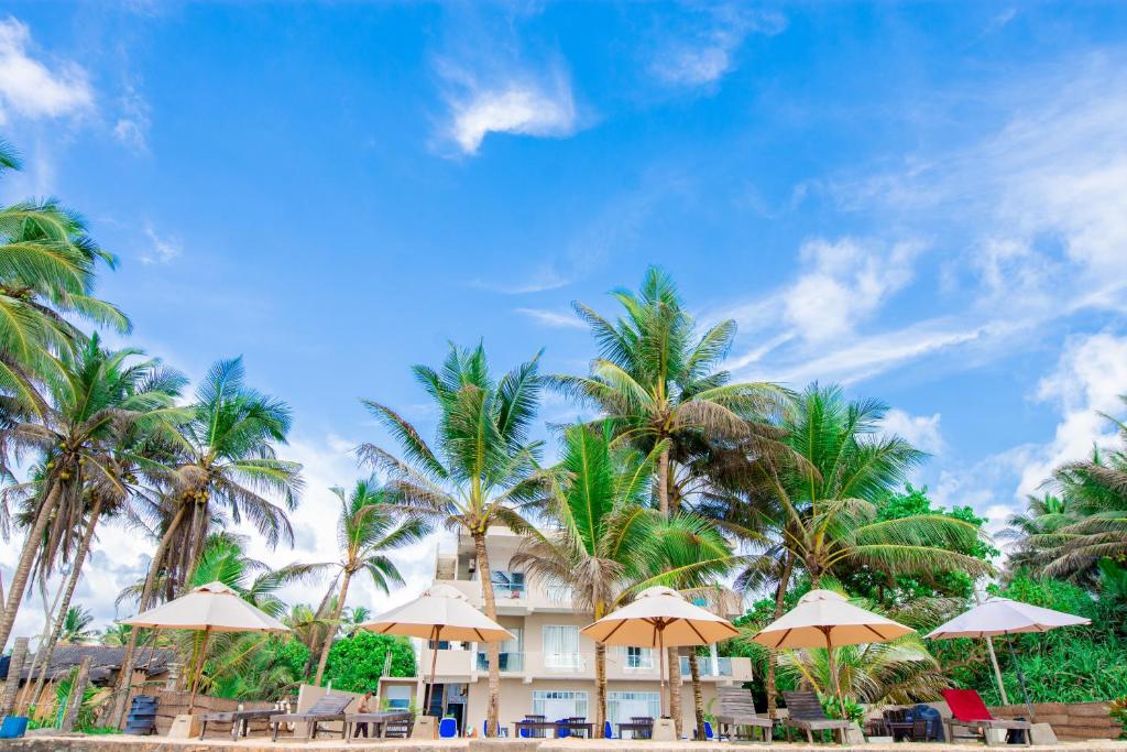 un hotel sulla spiaggia con palme e ombrelloni di Nico Beach Hotel a Hikkaduwa
