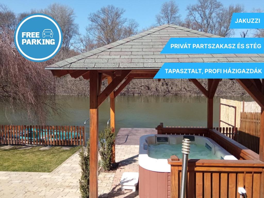 a wooden gazebo with a hot tub next to a river at Arborétum Nyaraló Szarvas - Kültéri jakuzzival in Szarvas