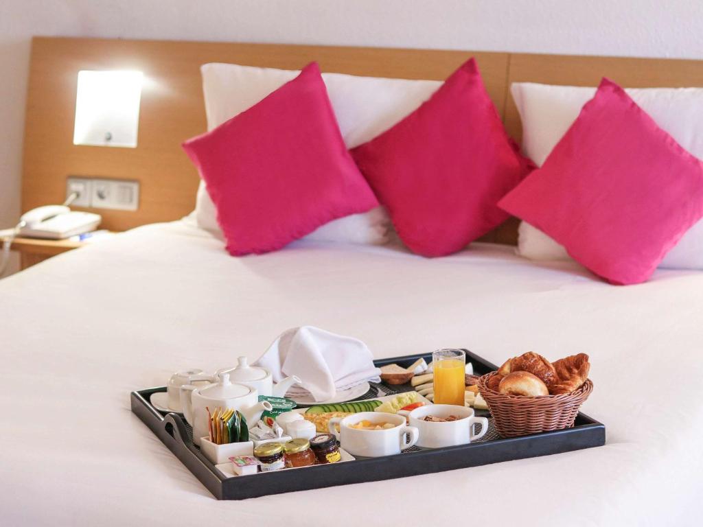 un vassoio con prodotti per la colazione su un letto con cuscini rosa di Novotel Tunis a Tunisi