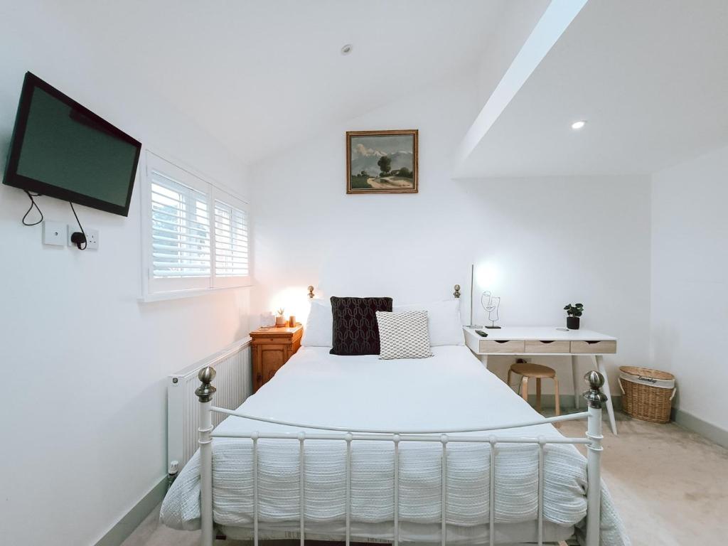 a white bedroom with a bed and a tv at The Pembroke Studio By Richmond Park in Kingston upon Thames