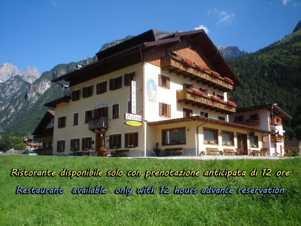 un bâtiment dans un champ avec des montagnes en arrière-plan dans l'établissement Hotel Galeno, à Auronzo di Cadore