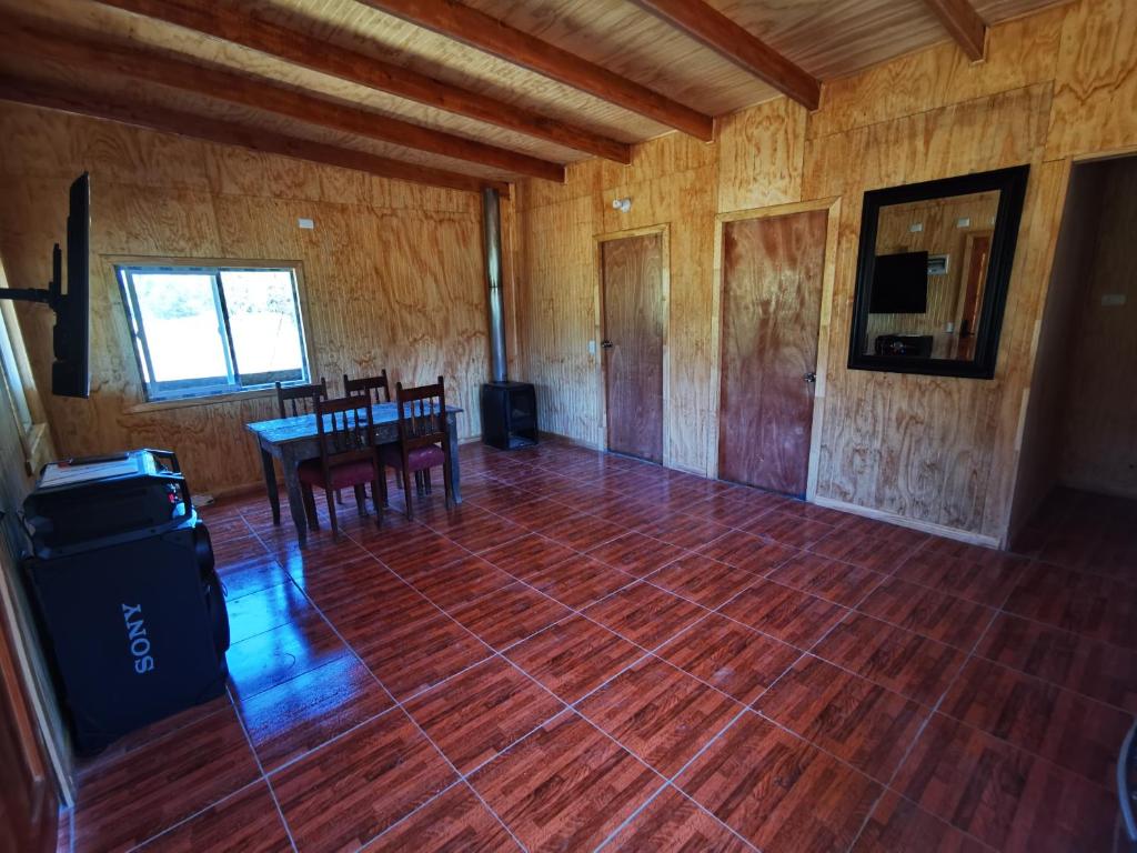 Habitación con suelo de madera, mesa y sillas. en Cabañas Orillas Del Nilahue, en Riñinahue