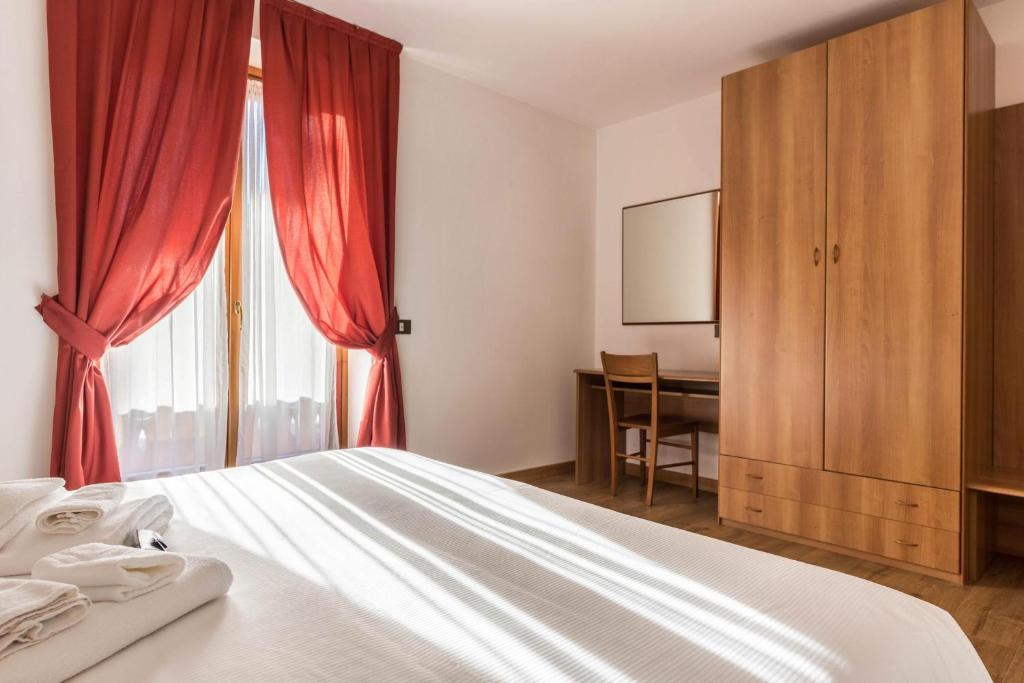 1 dormitorio con 1 cama con cortinas rojas y escritorio en Residence Park Imperator Bilocale 1, en Carisolo