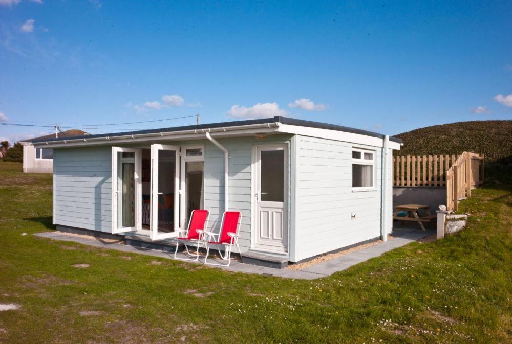 a white shed with two red chairs in a yard at A02 Mermaids Nest A2, Riviere Towans in Hayle