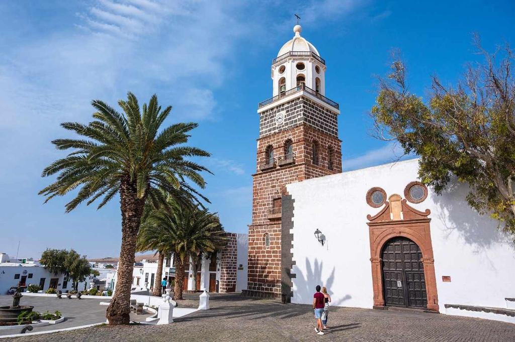 a woman walking in front of a building with a tower at CASA YOOJ designers house in teguise in Teguise