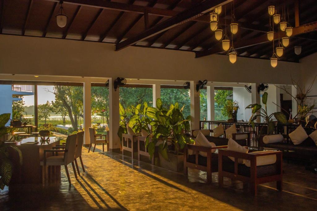 a restaurant with tables and chairs and windows at Sigiriya Wewa Addara Hotel - Hotel By The Lake in Sigiriya