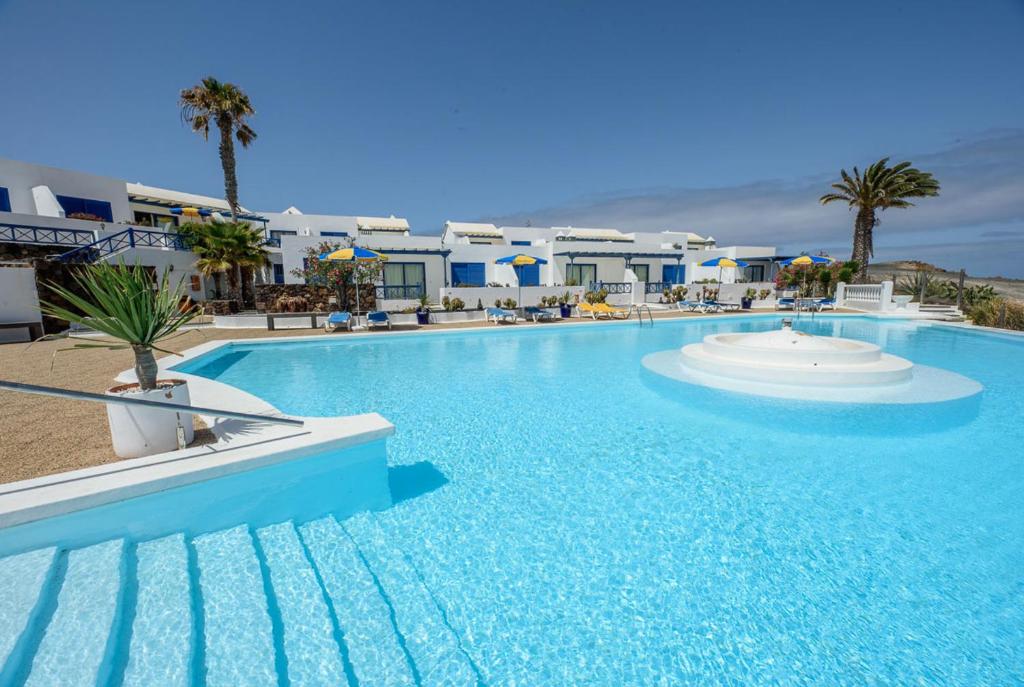 a large blue swimming pool with palm trees and buildings at Oböna Castillo de Papagayo, Complejo Nudista FKK-Nudist Resort in Charco del Palo