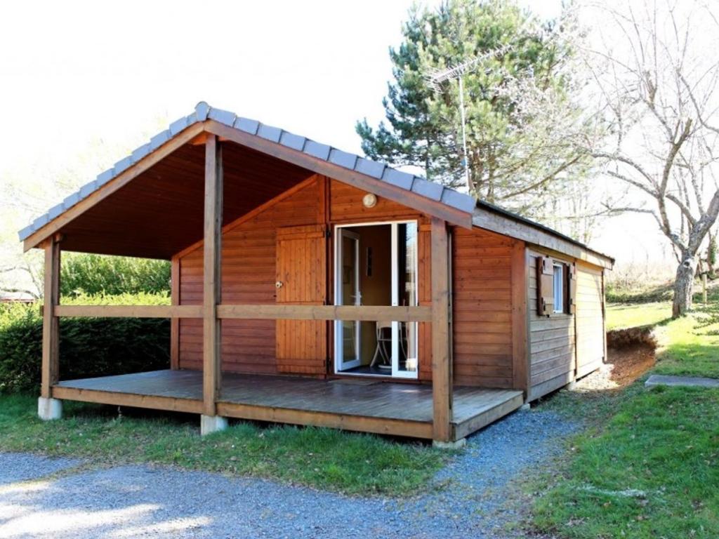 małą drewnianą kabinę z gankiem w trawie w obiekcie Chalets indépendants en camping 2 étoiles avec terrasse – Idéal famille, activités et jeux pour enfants - FR-1-489-405 w mieście Treignat