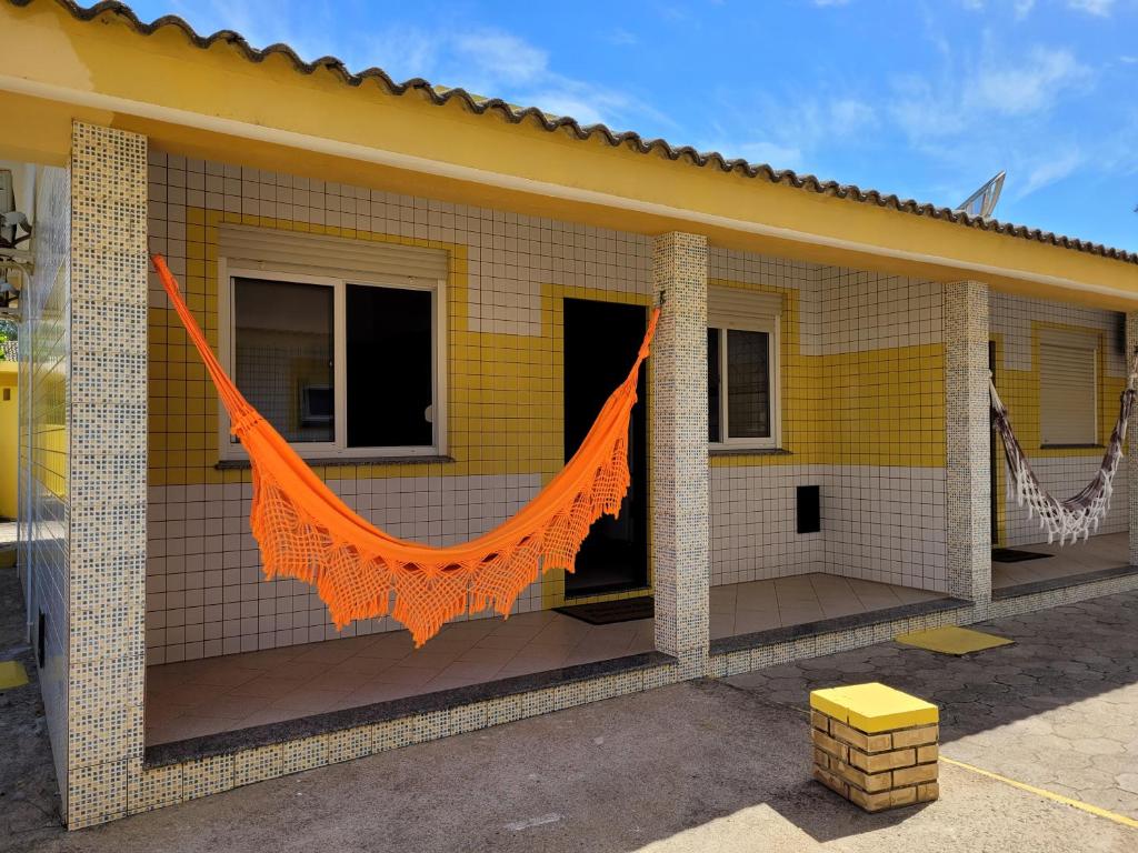 Una casa amarilla con una red naranja. en Pousada Genoveva - Apto com dois dormitórios, en Laguna