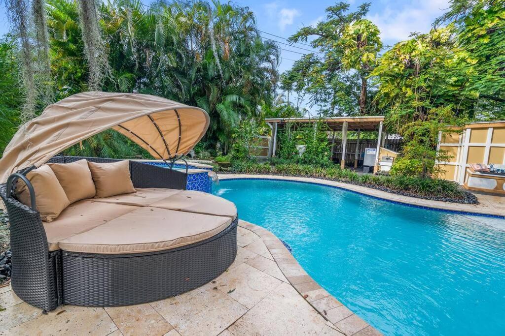 a wicker chair with an umbrella next to a swimming pool at Tropical Oasis Located Near Lake With Pool and Hot Tub in West Palm Beach