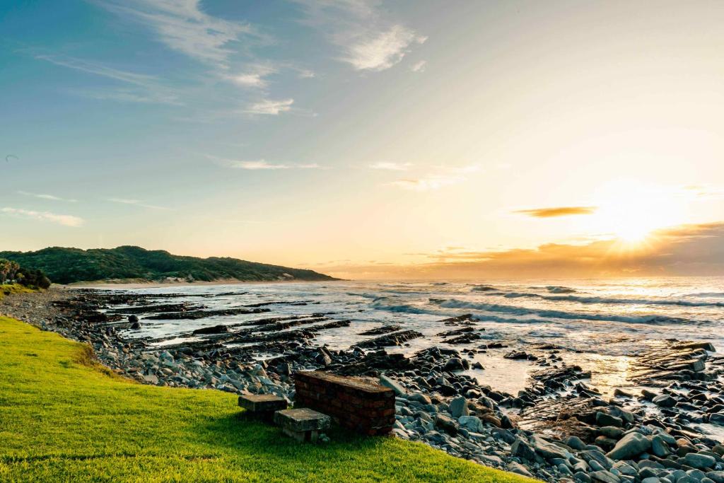 una playa con rocas y el océano con una puesta de sol en Mitford Lodge, en Morganʼs Bay