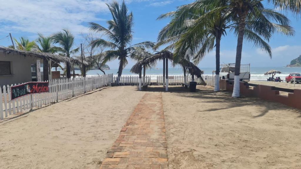 Casa a pie de playa isla de la piedra في مازاتلان: شاطئ رملي به نخيل وسياج أبيض