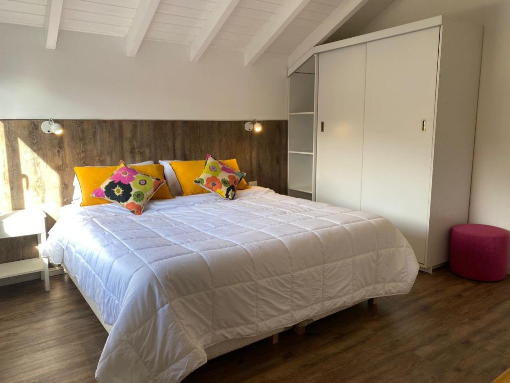 1 dormitorio con 1 cama blanca grande con almohadas coloridas en ALOJAMIENTOS PATAGONICOS Las Mosqueteras Duplex vla en Villa La Angostura