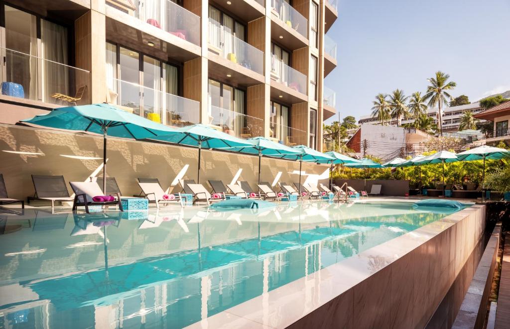 uma piscina num hotel com cadeiras e guarda-sóis em GLOW Mira Karon Beach em Praia de Karon