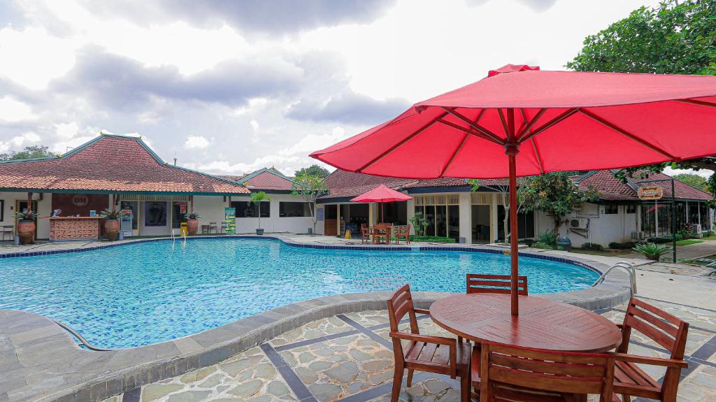 a table with a red umbrella next to a pool at Royal Brongto Hotel in Timuran