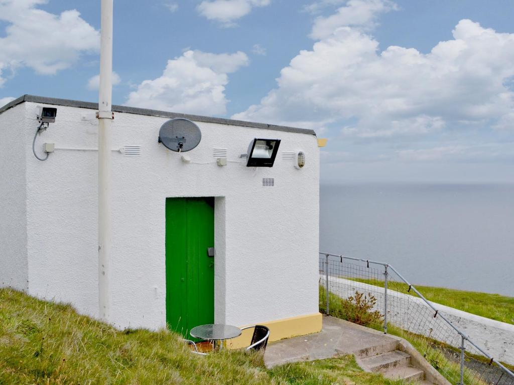 a small white building with a green door on a hill at St Abbs The Flag House in Saint Abbs