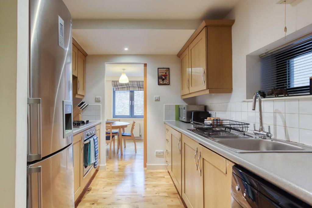 a kitchen with wooden cabinets and a stainless steel refrigerator at *Amazing Location!*In heart of the City. 2BR & Cot in Edinburgh