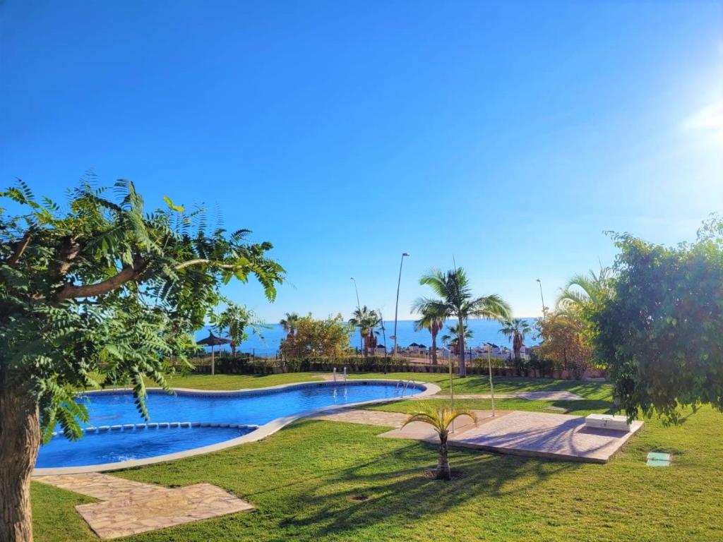 een zwembad in een park met palmbomen bij Espacioso apartamento con preciosos jardines y BBQ in Isla Plana