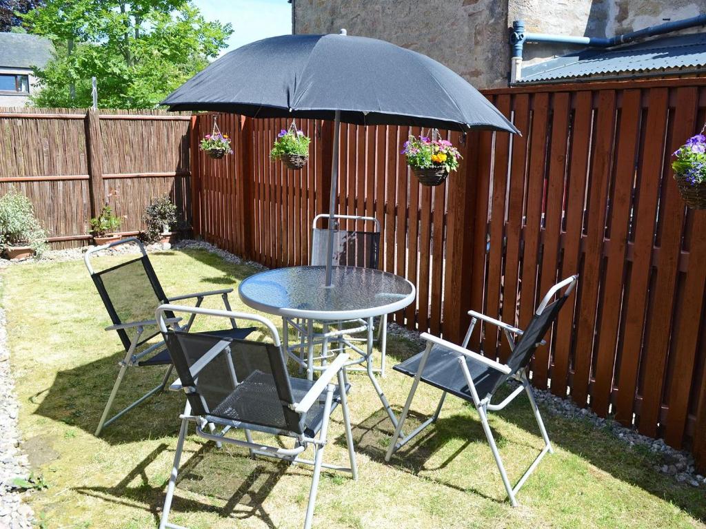 una mesa y sillas bajo una sombrilla en un patio en Acorn Cottage en Cononbridge